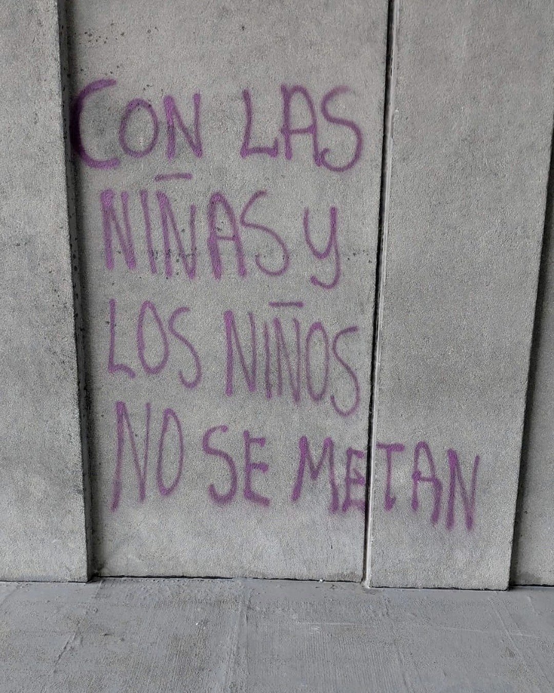 Pinta morada sobre concreto que dice Con las niñas y los niños no se metan.